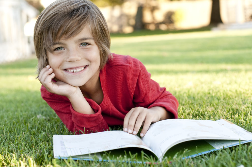 boy lying on the grass reading a kids book